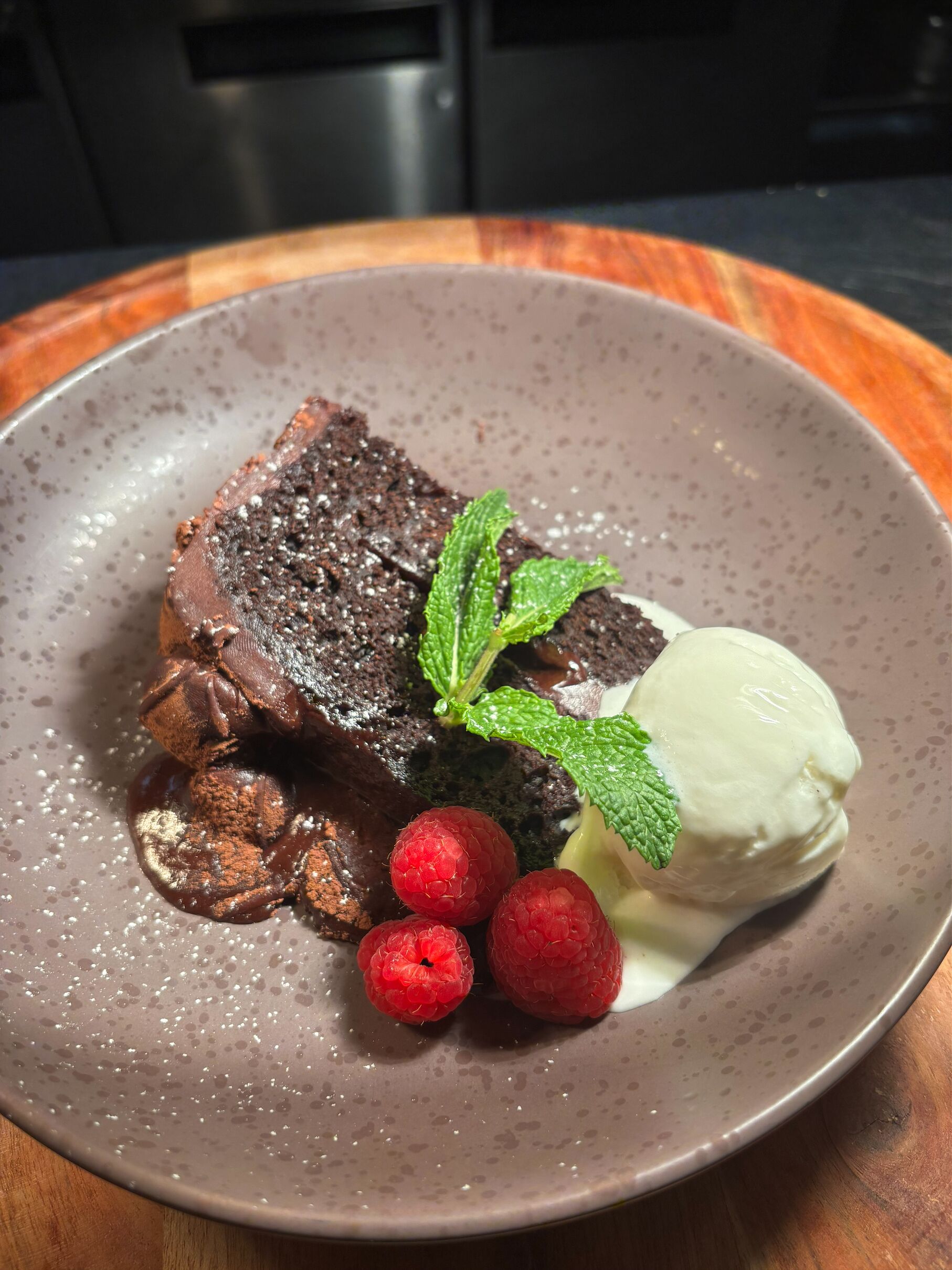 Un plato de postre con un brownie, frambuesas, menta y una bola de helado.