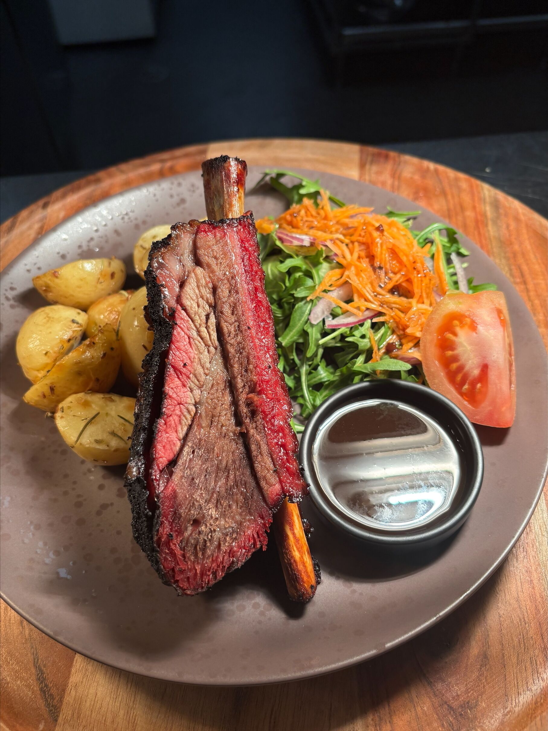 A plate with a grilled steak, roasted potatoes, a salad, and a tomato slice.