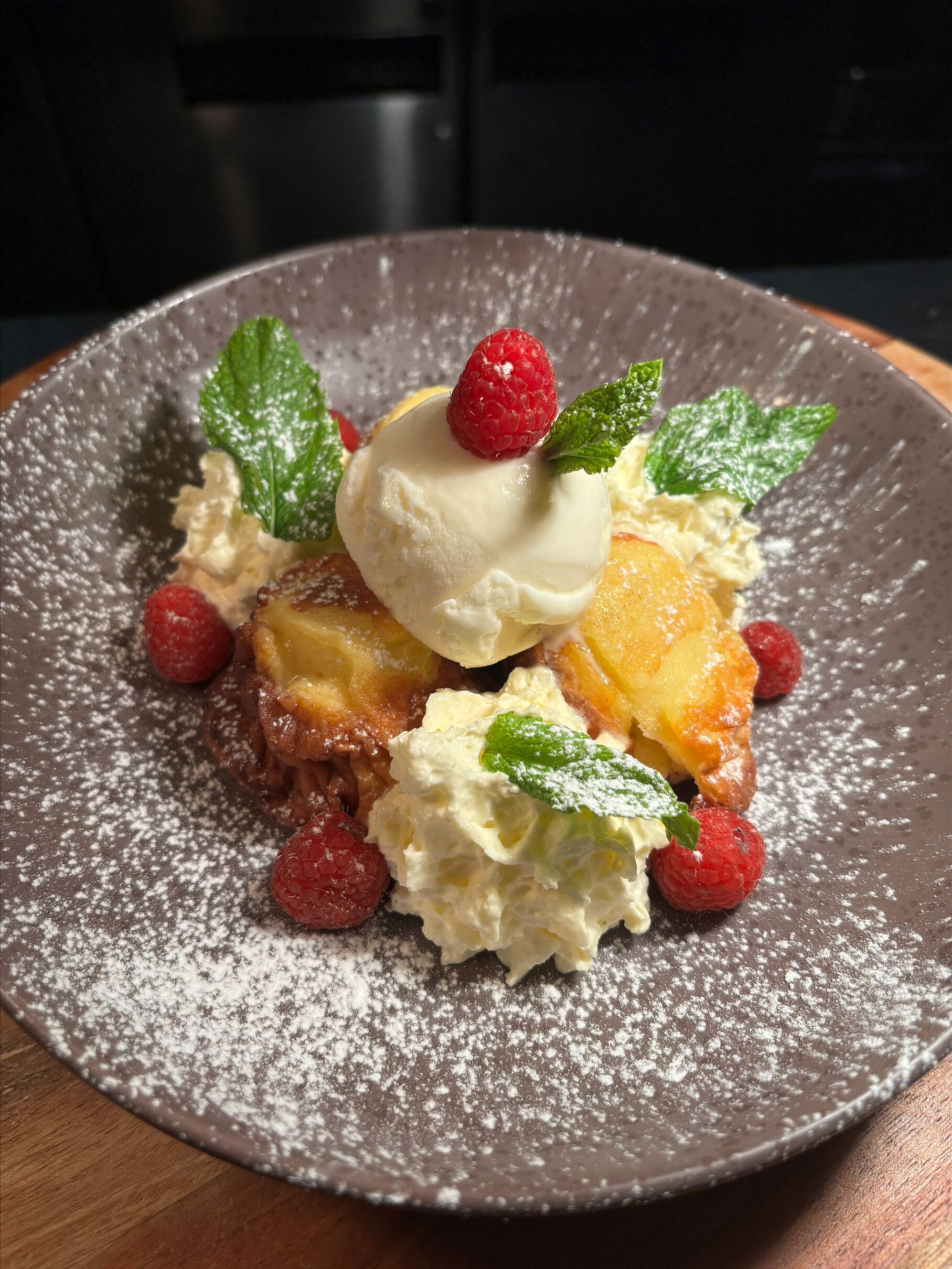 A dessert plate with a scoop of ice cream, raspberries, and mint leaves.