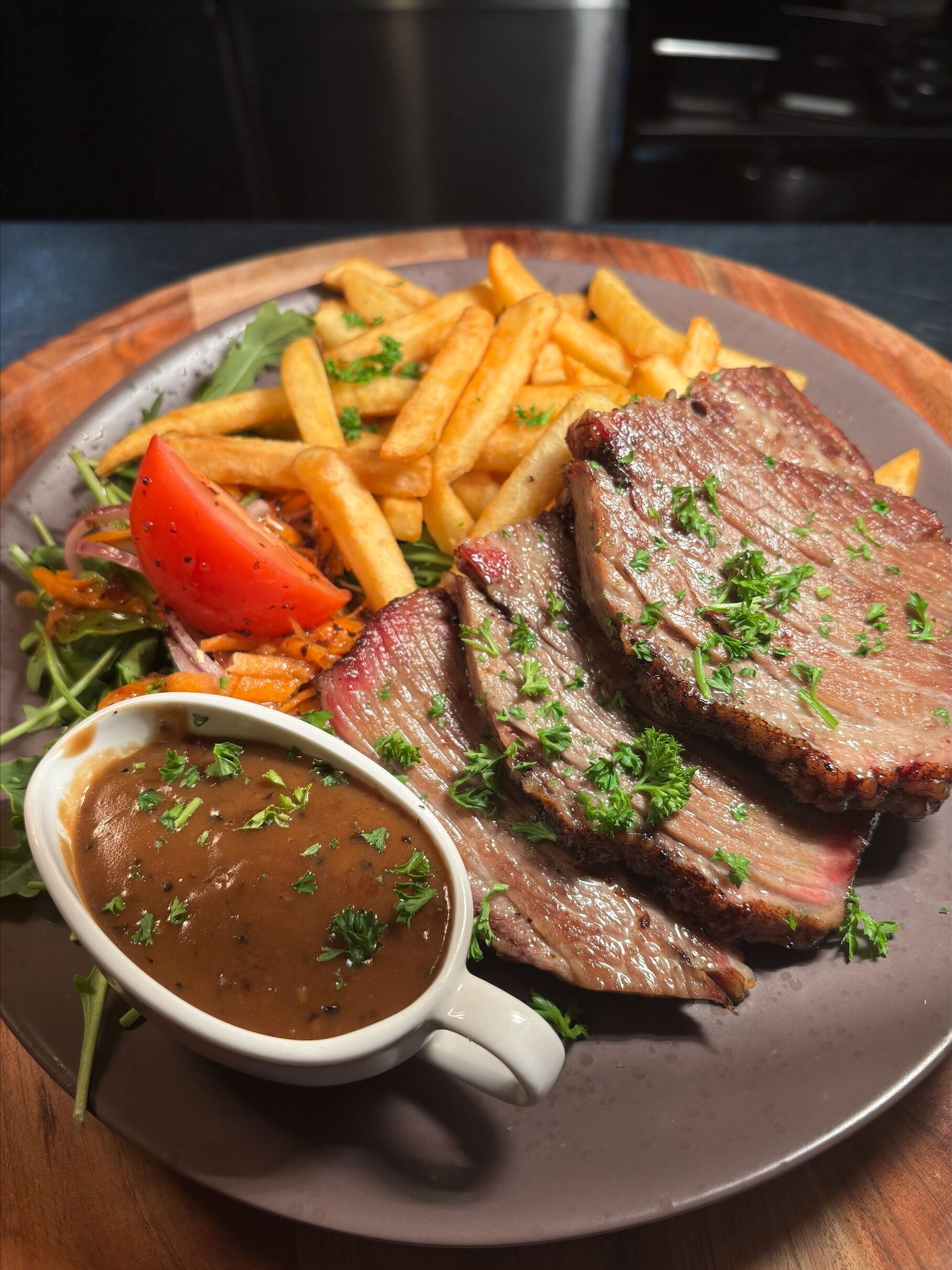 En tallerken med bøf, pommes frites, en tomat og en lille skål med sauce.