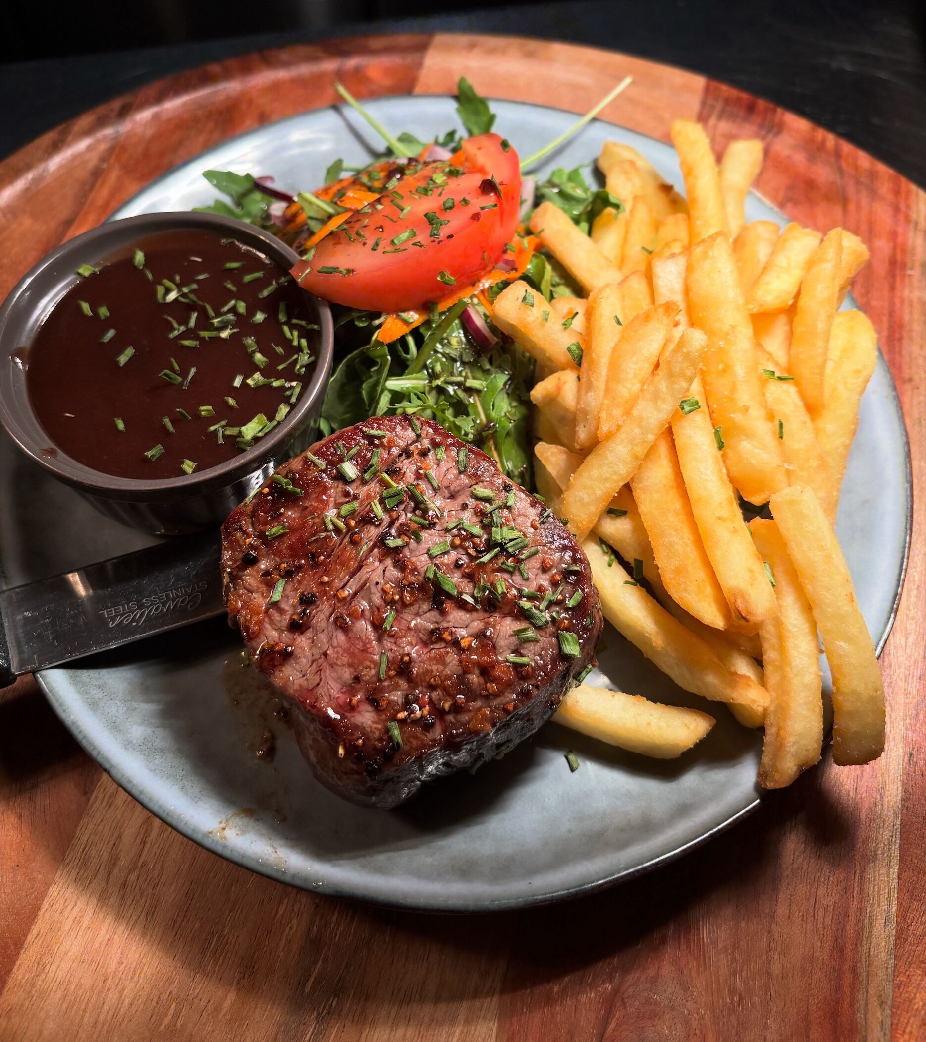A plate with a steak, fries, a tomato, and a side salad.