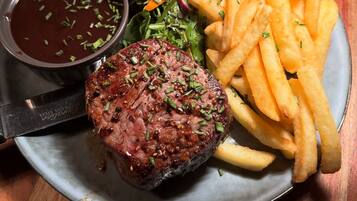 A plate with a steak, fries, a tomato, and a side salad.
