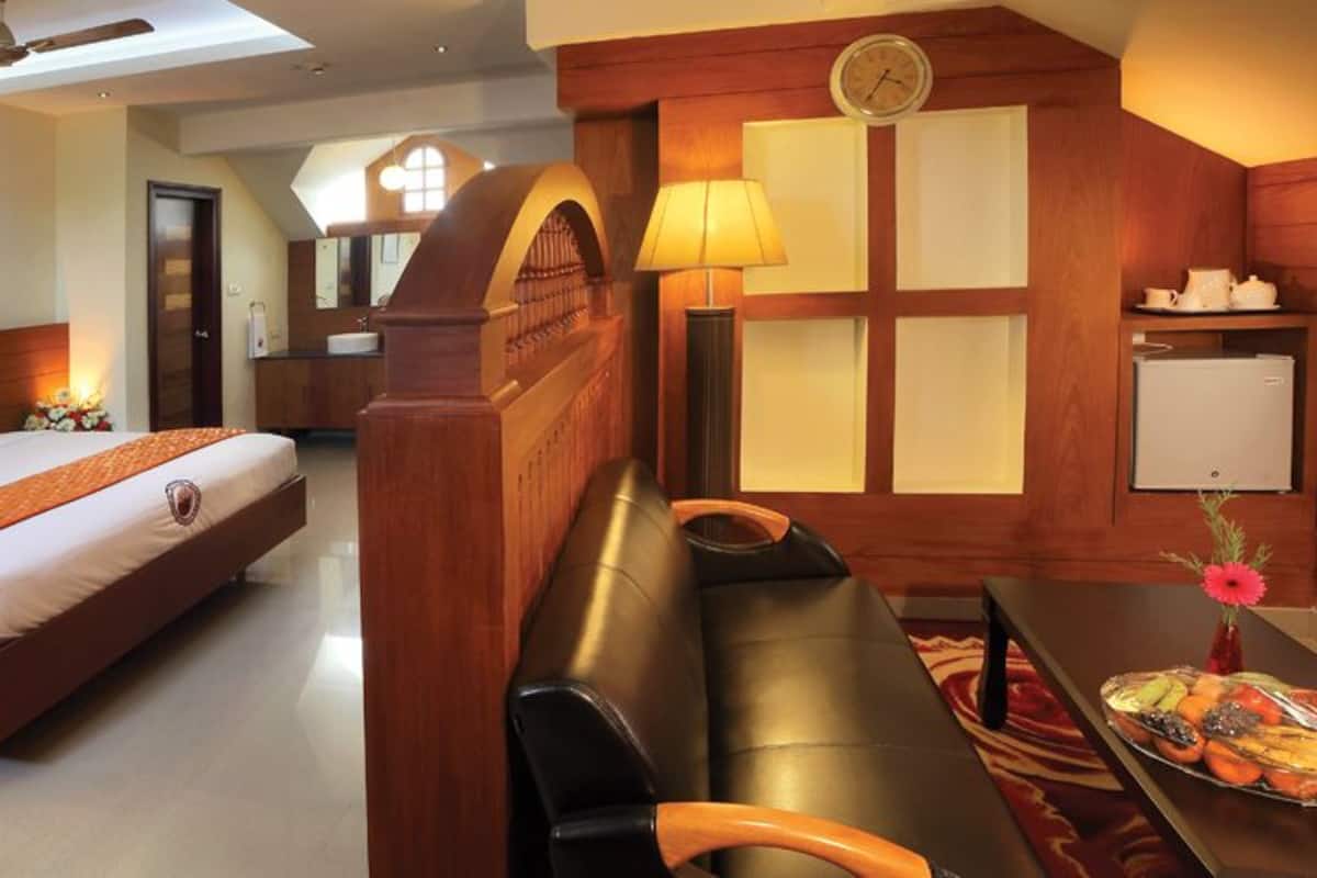 Quarto de hotel com uma cama grande, uma escrivaninha, uma cadeira, uma mesinha de centro com um vaso e um relógio na parede.