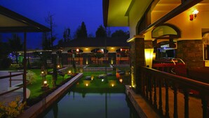 A nighttime view of a hotel with a swimming pool, outdoor seating, and a well-lit entrance. - Wetzlar Resorts and Hotels (Muvattupuzha)