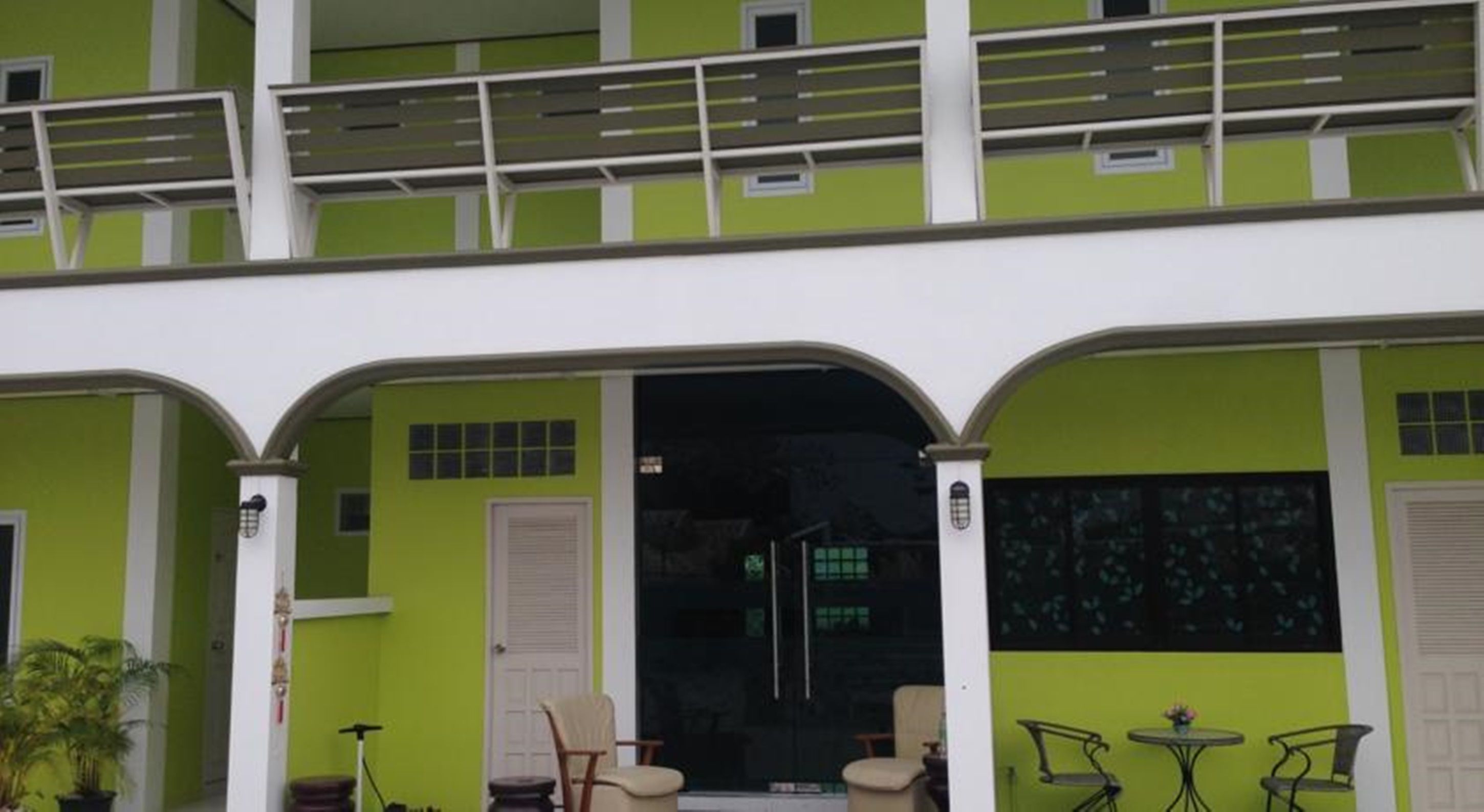 A two-story building with a green facade, a balcony, and a glass door entrance.