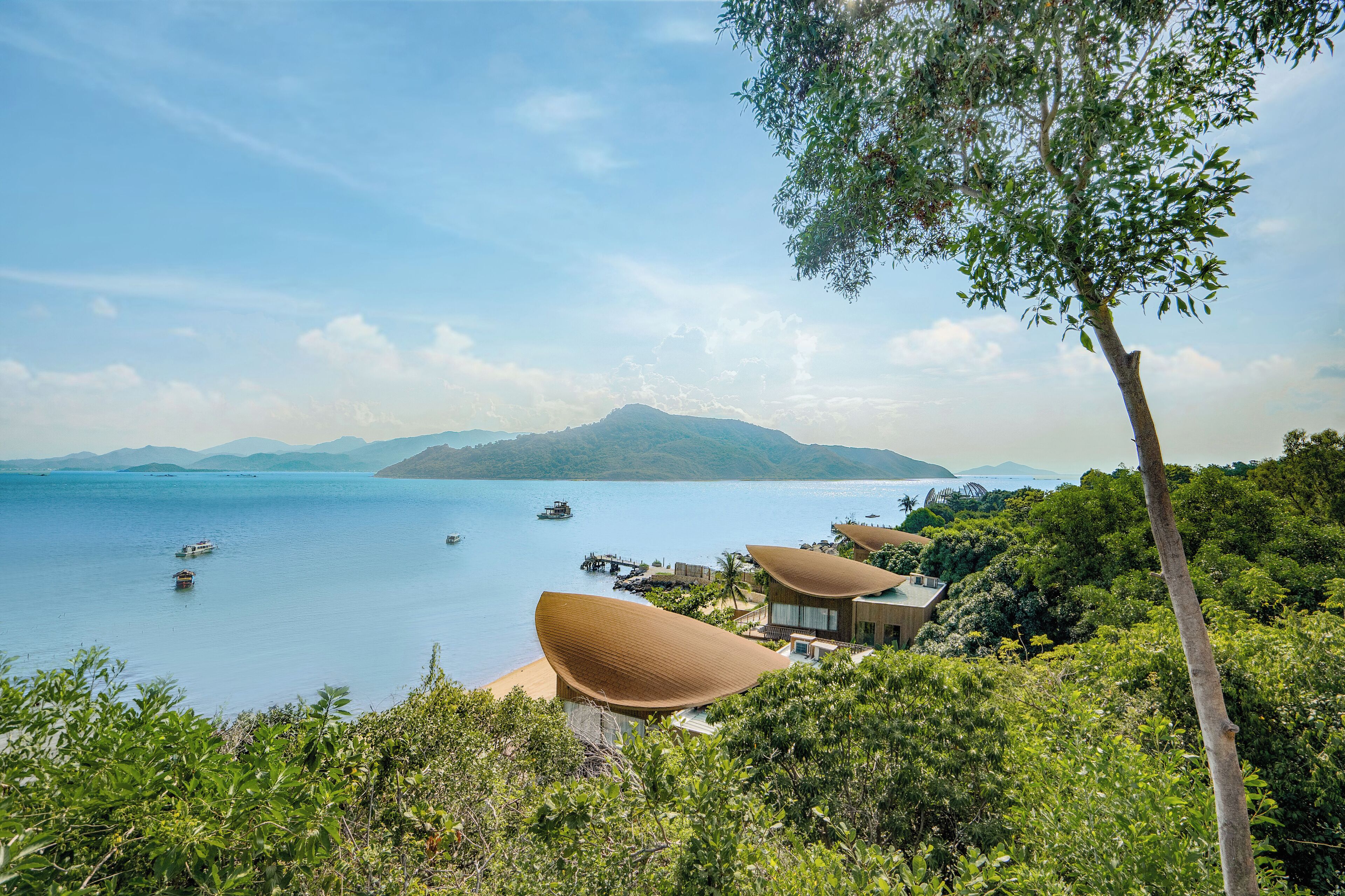 A coastal resort with modern architecture, a clear view of the sea, and a mountainous backdrop.