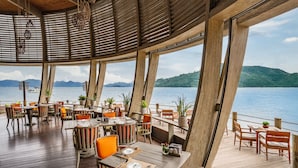 Een terras met houten tafels en stoelen, plantenbakken en uitzicht op het water en de bergen.