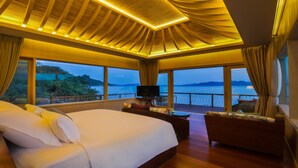 Een ruime slaapkamer met een groot bed, een televisie en een balkon met uitzicht op zee.