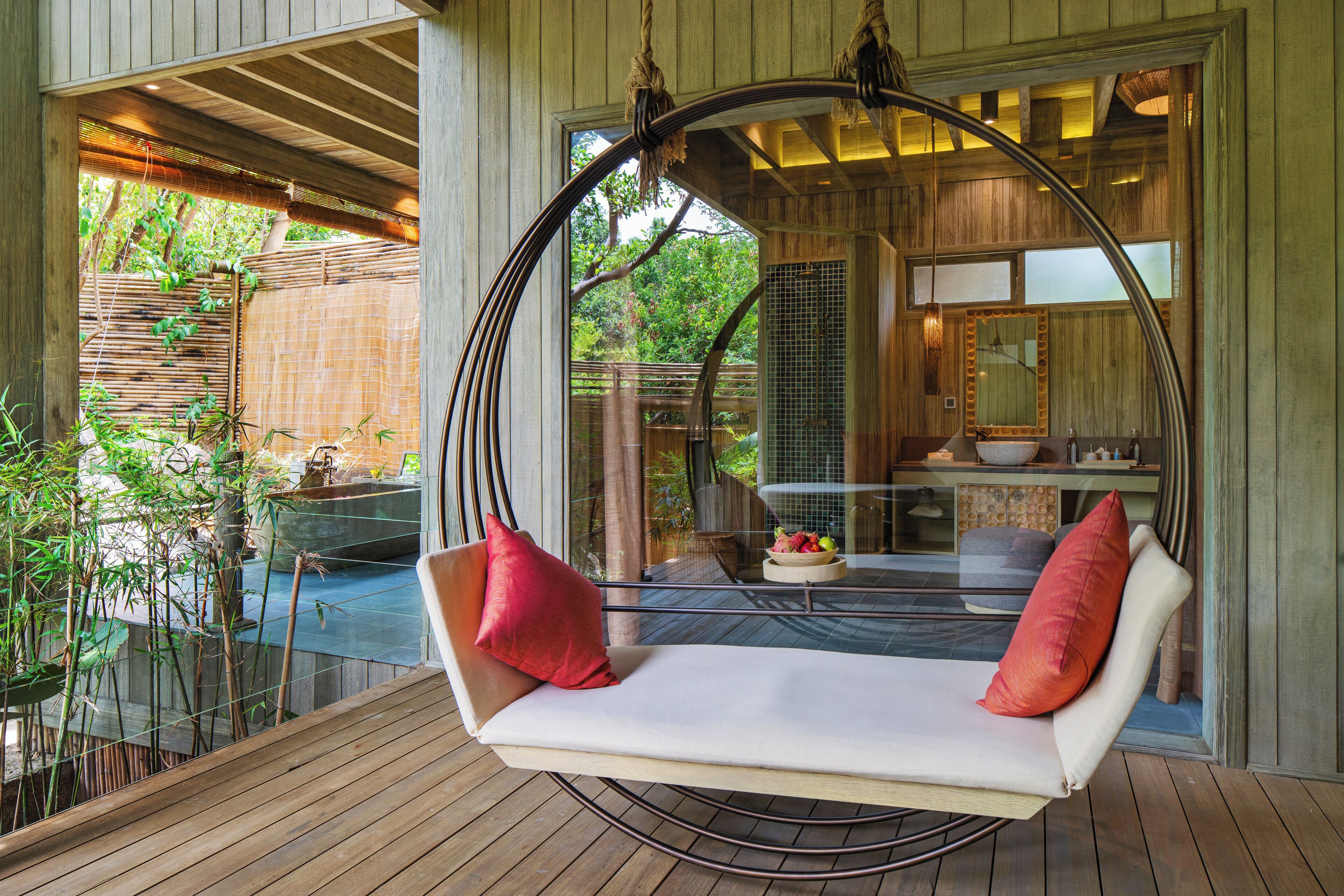 Terraza de madera con una silla colgante y vistas a una piscina y jardín.