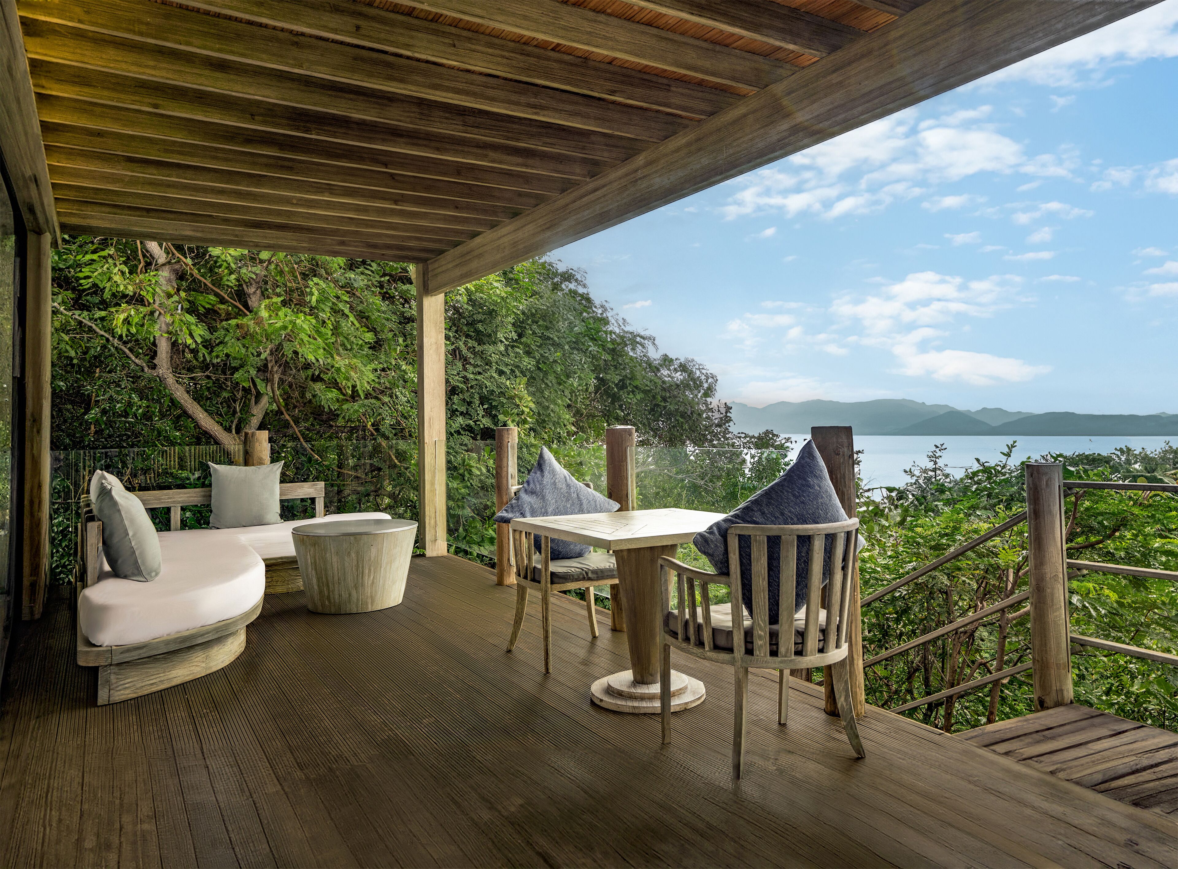 A wooden deck with a table and chairs, overlooking a lake and mountains.
