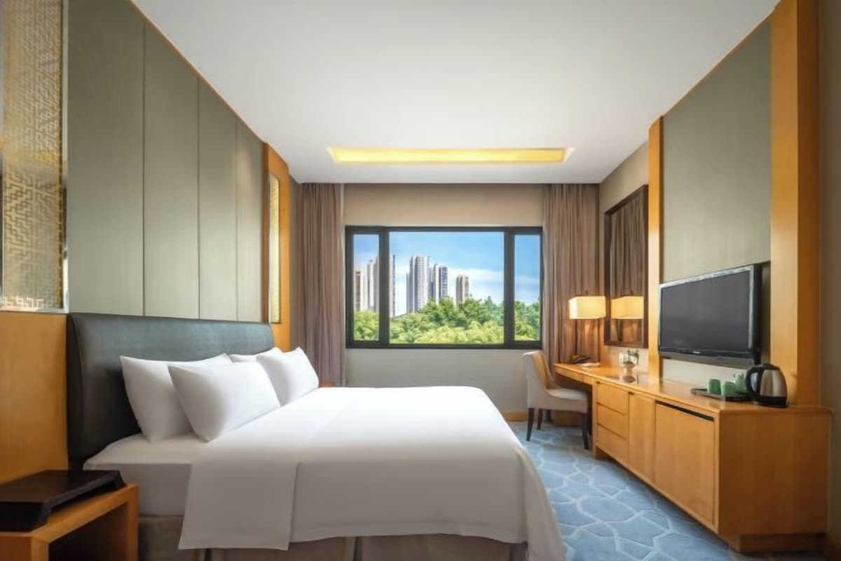 Habitación de hotel con cama, escritorio con televisor, una silla y ventana con vista a la ciudad.