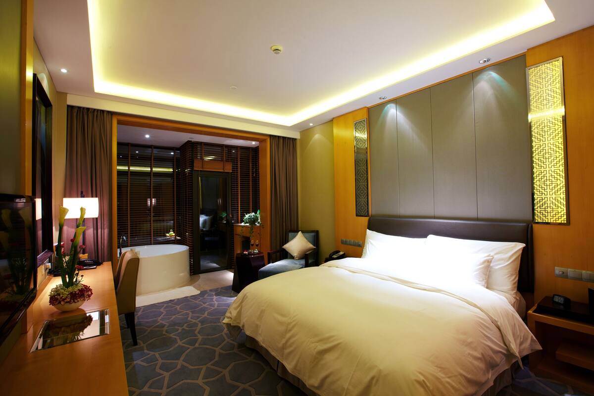 Een hotelkamer met een groot bed, een bureau met een lamp, een stoel en een badkamer met een bad.