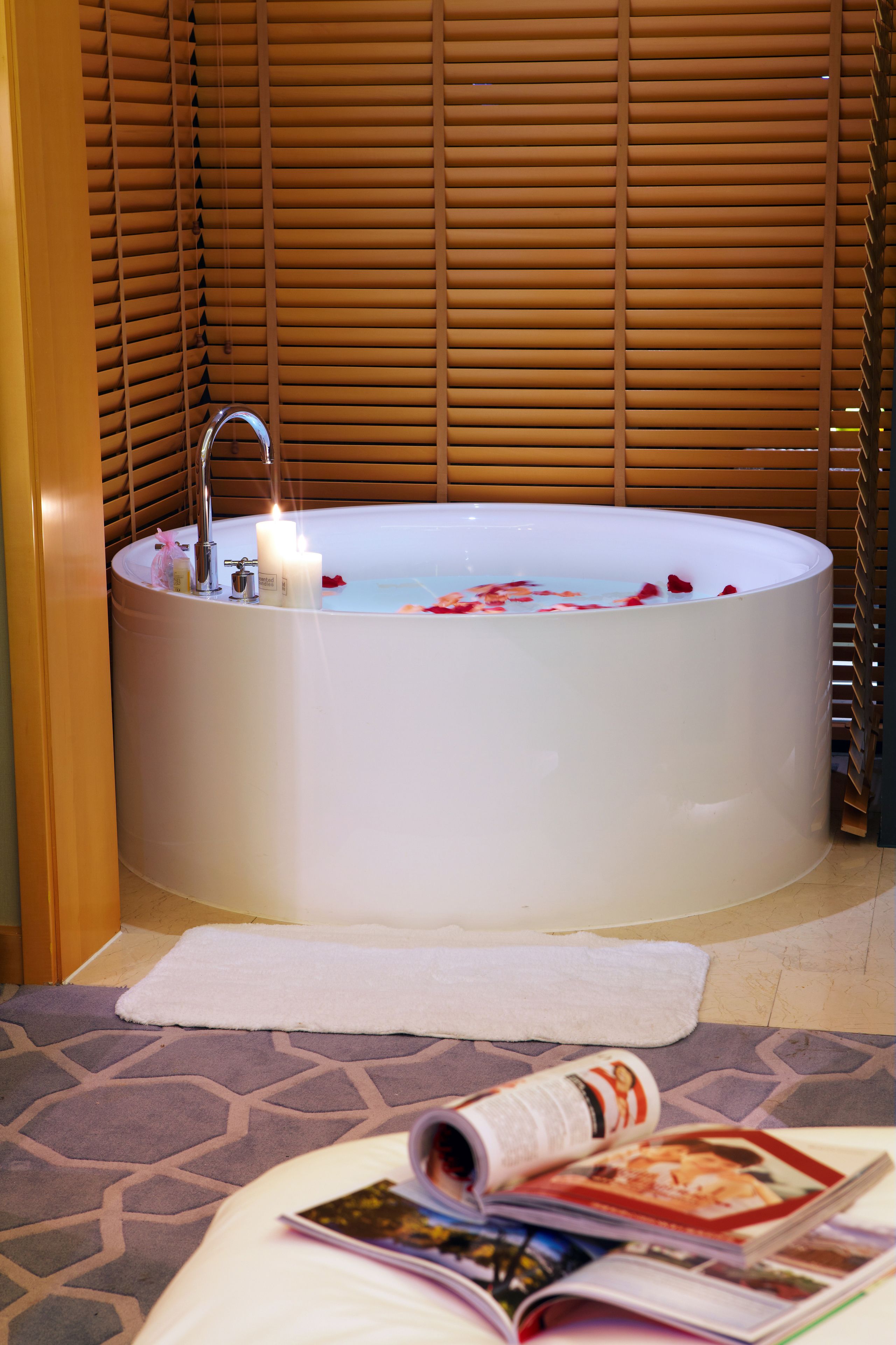 Una bañera con pétalos de rosa, una vela y una revista sobre una toalla.