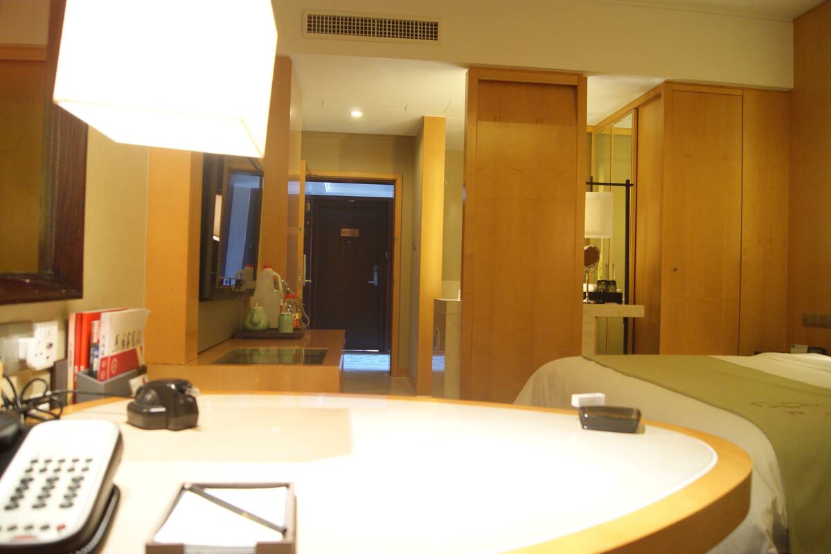 Een hotelkamer met een rond wastafel, een spiegel, een bed en een deur naar een gang.