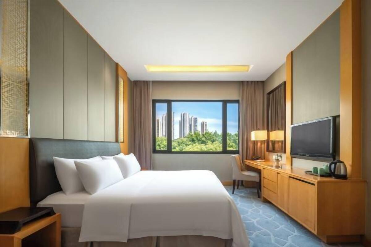 Een hotelkamer met een bed, een bureau met een televisie, een stoel en een raam met uitzicht over de stad.