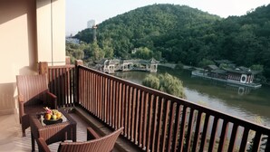 Een balkon met rieten meubels en een schaal fruit. In de achtergrond is een rivier met traditionele gebouwen en een brug te zien.