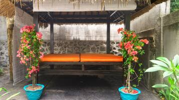 Relax in a serene outdoor space with a thatched roof, wooden bench, and lush greenery.