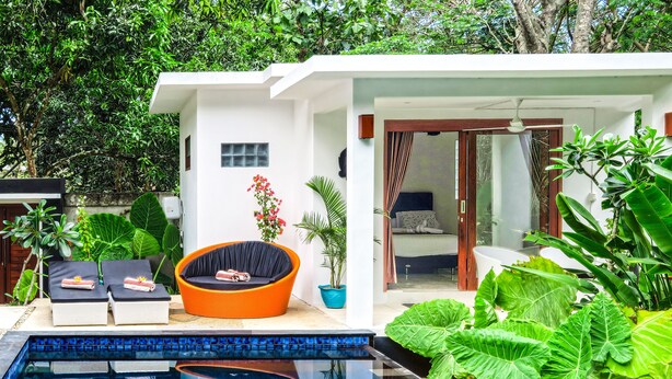 A modern outdoor pool area with lounge chairs, a small orange chair, and lush greenery. - Villa Collard (Senggigi)