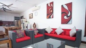 A modern living room with grey sofas and red cushions, a glass coffee table, and abstract wall art. - Villa Collard (Senggigi)