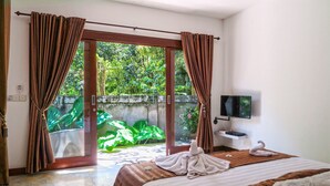 A hotel room with a bed, curtains, a TV, and a view of greenery outside. - Villa Collard (Senggigi)