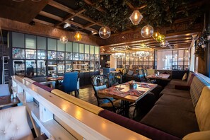 Een restaurant met houten balken, hangende吊灯 en verschillende zitmogelijkheden, waaronder zithoeken en tafels.