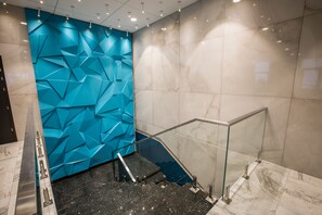 Een modern interieur met een blauwe muur met geometrische patronen, marmeren vloer en een glazen balustrade op een trap.