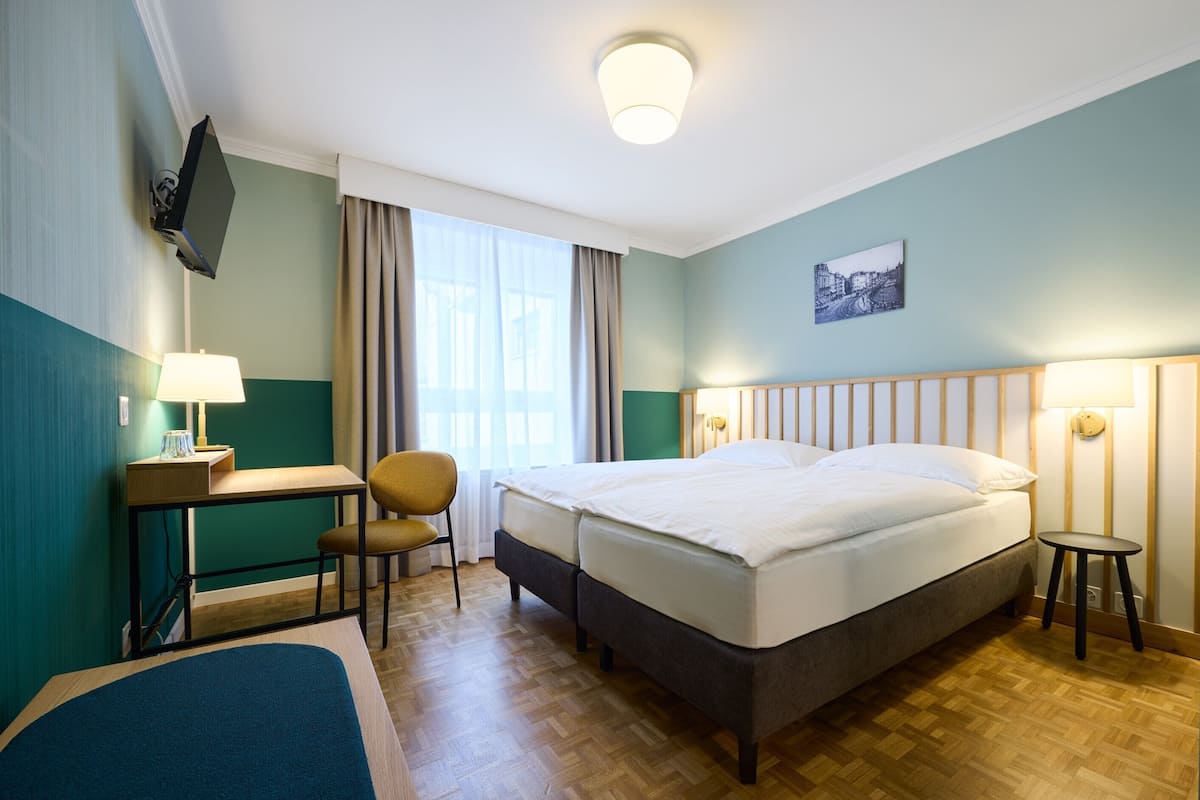 Hotellihuone, jossa on sänky, työpöytä, tuoli, televisio ja ikkuna, jossa on verhot.