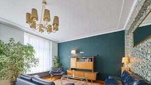 Una sala de estar con un sof á azul, un sofá de cuero oscuro, un aparador de madera con libros, una planta en maceta y un candelabro.
