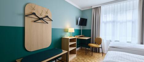 Quarto de hotel com cabeceira de madeira, escrivaninha com luminária, televisão, cadeira e cama.