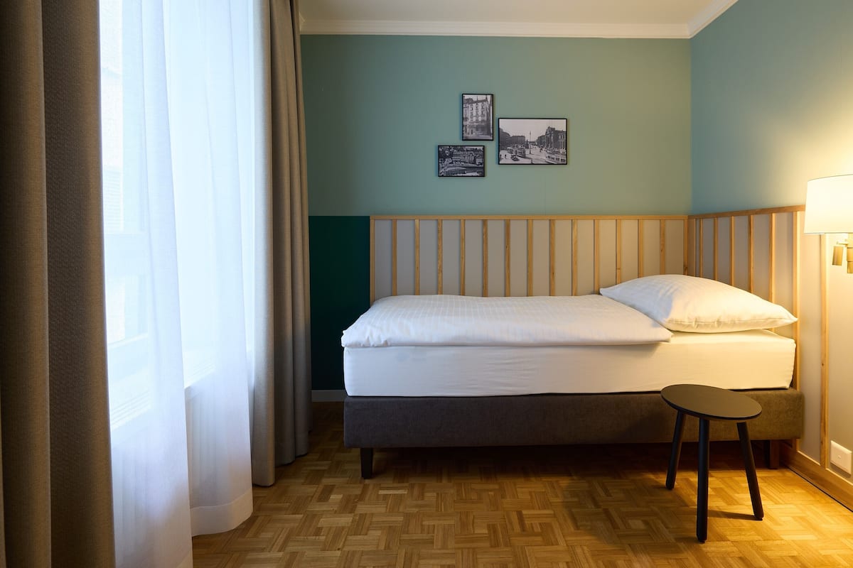 Hotellihuone, jossa on sänky, pieni jakkara ja kolme kehystettyä kuvaa seinällä.