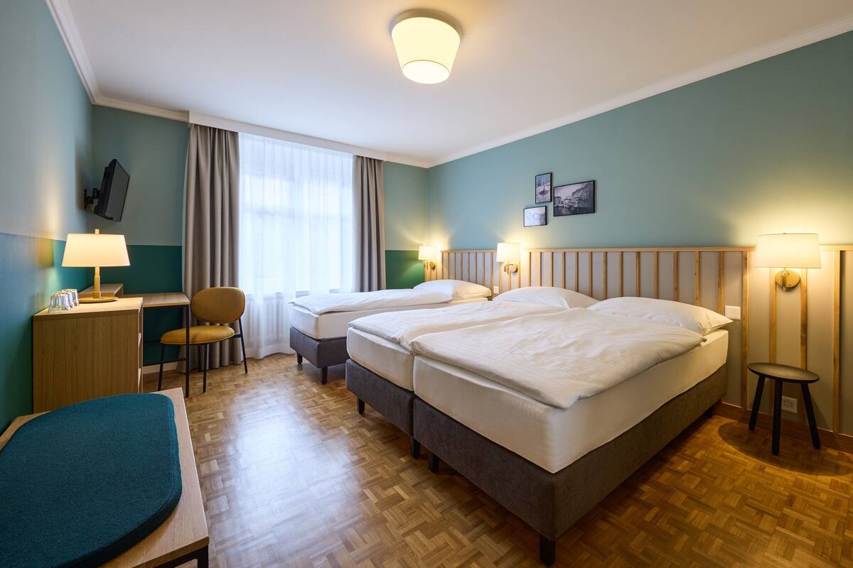 Hotellihuone, jossa on kaksi sänkyä, työpöytä tuolilla, pieni pöytä ja lamppu.