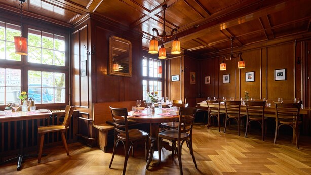 Un restaurante con suelos de madera, ventanas amplias y lámparas colgantes.