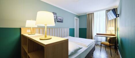 Una habitación de hotel con una cama, un escritorio, una silla, un televisor y una lámpara.