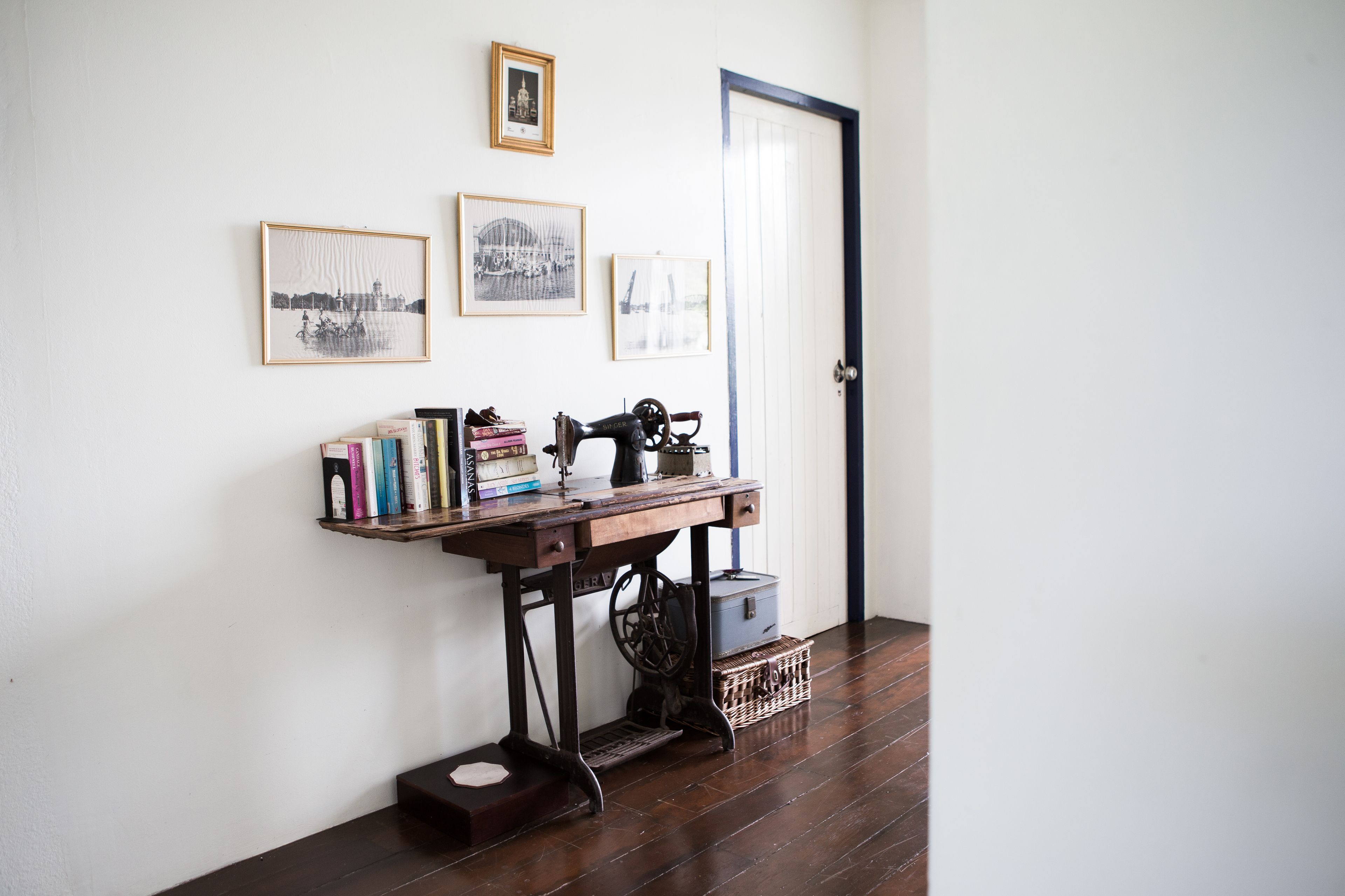 Una habitación con una mesa de madera junto a una pared blanca, donde hay libros y una máquina de coser.