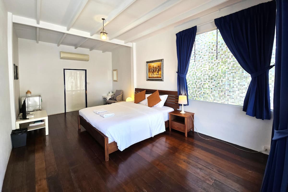 A spacious bedroom with a large bed, a bedside table, a nightstand, and a window with curtains.