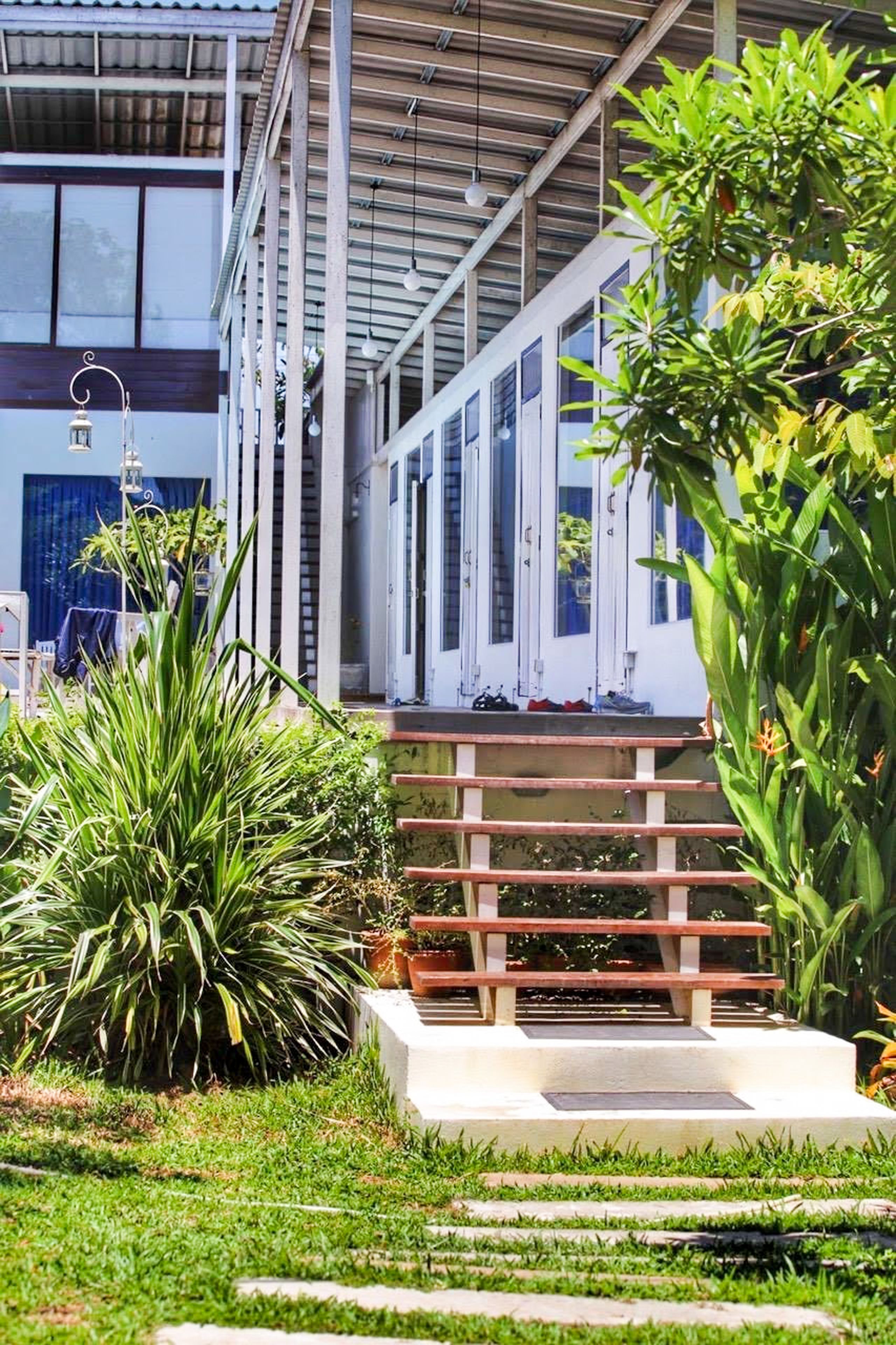 Un edificio moderno con un acceso cubierto, escalones que conducen a una puerta y abundante vegetación circundante.