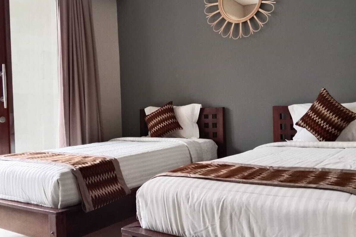 A bedroom with two beds, a large mirror, and a window with curtains.