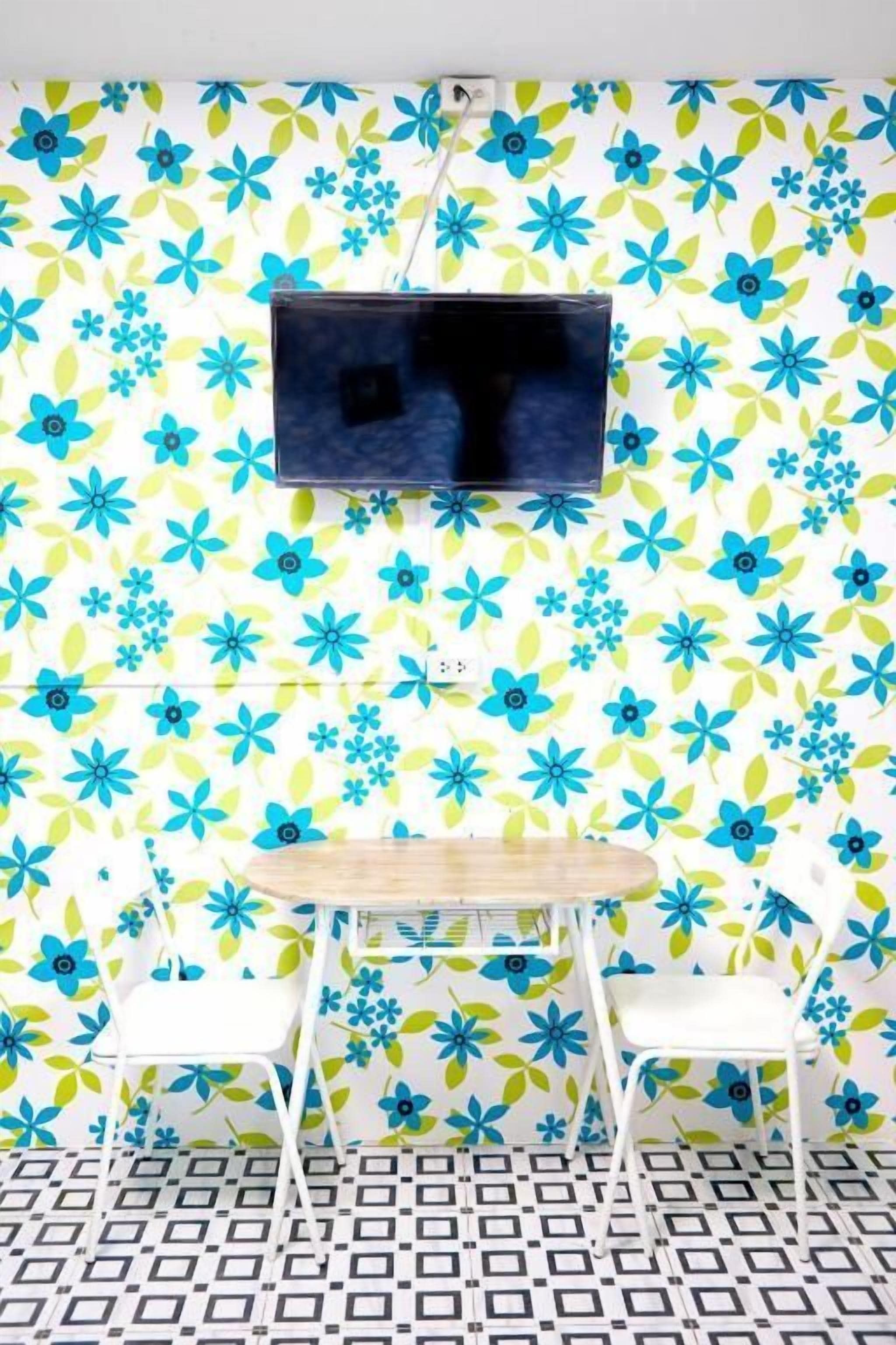 Ein Zimmer mit floraler Tapete, einem an der Wand montierten Fernseher, einem kleinen runden Tisch und zwei weißen Stühlen.
