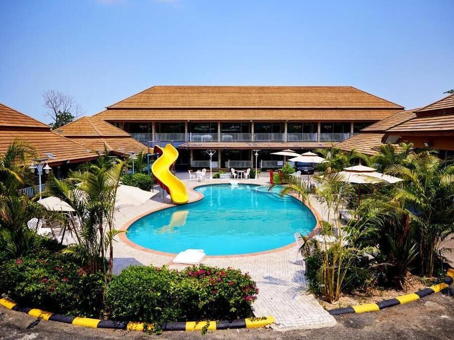 A swimming pool with a slide, surrounded by palm trees and a building with a tiled roof.