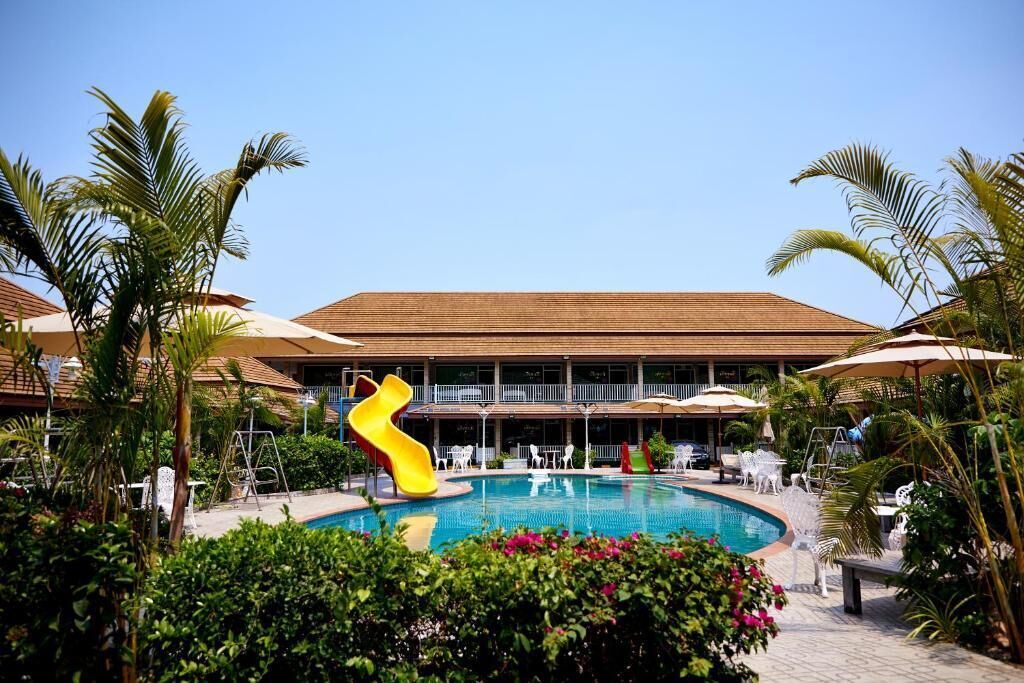 A pool area with a yellow slide, surrounded by palm trees and lounge chairs.