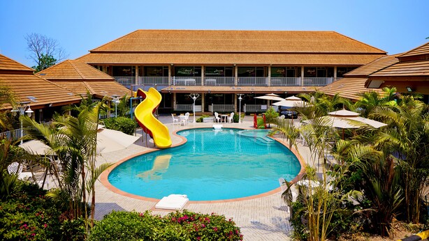 A swimming pool with a yellow slide, surrounded by palm trees and lounge chairs. - Baandara Resort Saraburi (Saraburi)