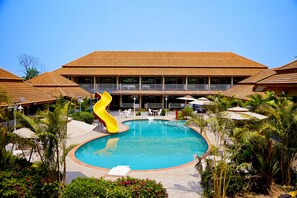 Piscina con un tobogán amarillo, rodeada de palmeras y sillones de descanso.