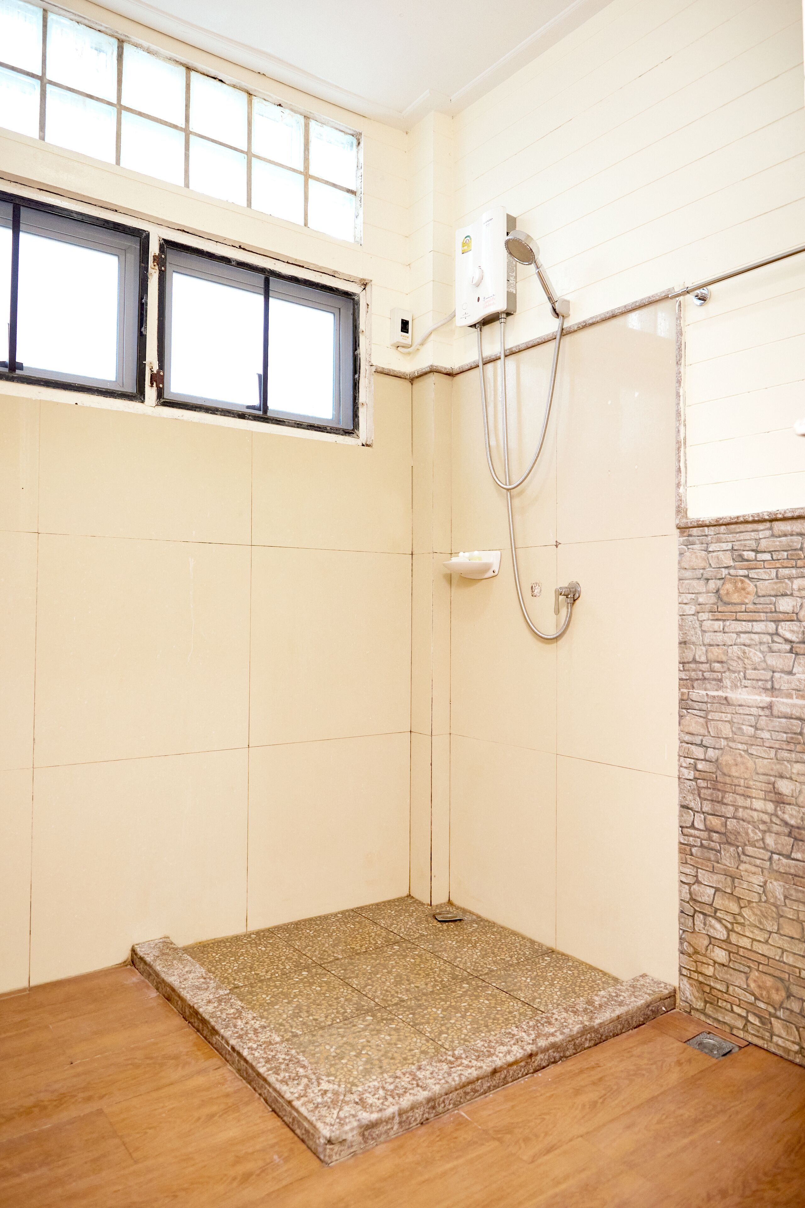 Un petit espace douche fermé, doté d’un sol carrelé et d’un mur en pierre.