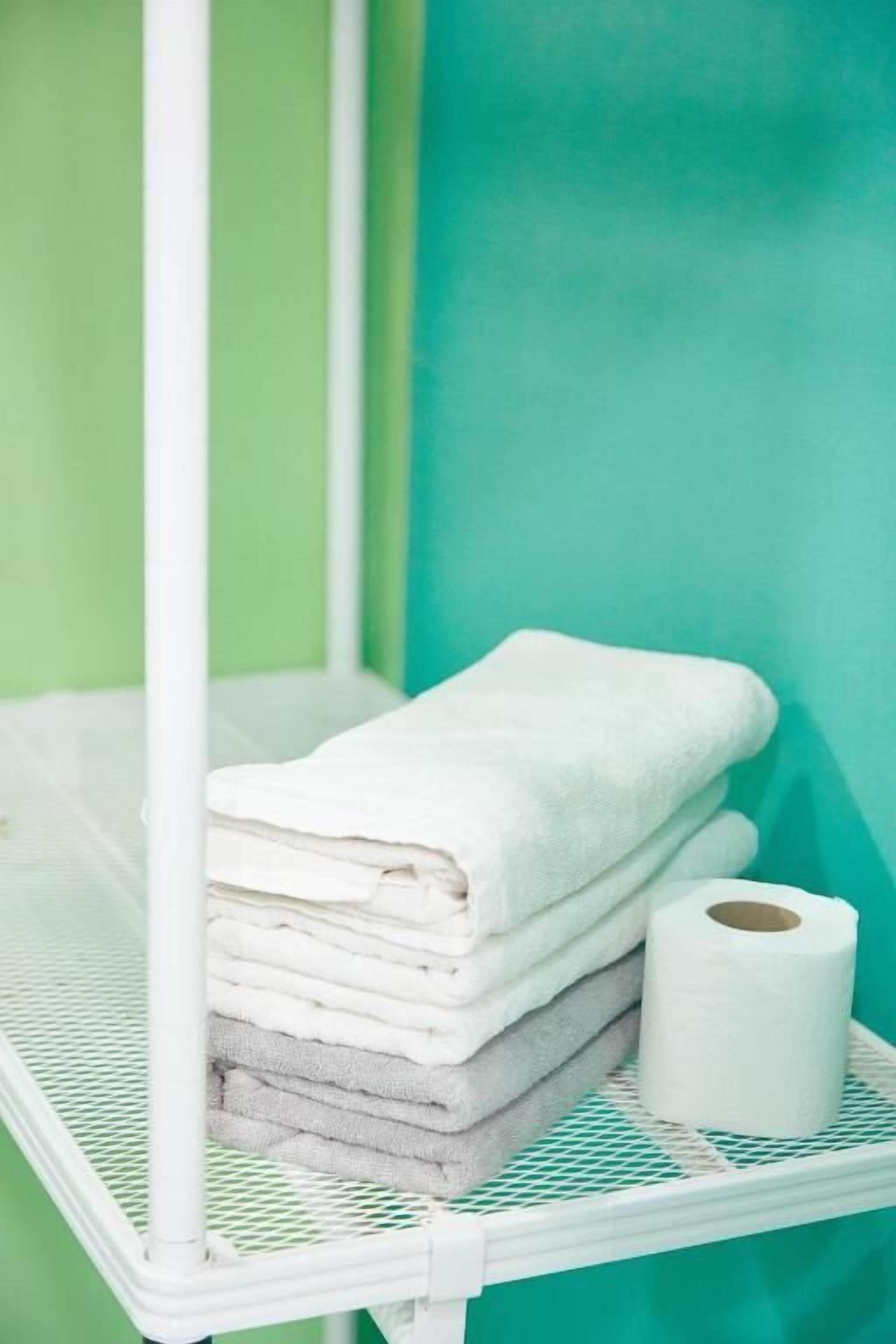 Une étagère en métal blanc sur laquelle sont pliées des serviettes blanches et posé un rouleau de papier toilette.