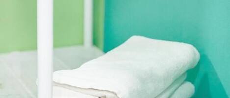 Une étagère en métal blanc sur laquelle sont pliées des serviettes blanches et posé un rouleau de papier toilette.
