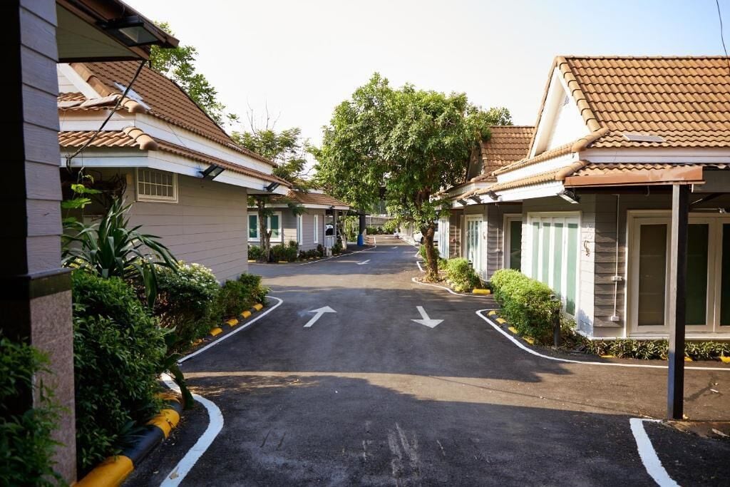Une rue résidentielle bordée de maisons des deux côtés, une chaussée dégagée avec des flèches indiquant le sens de la circulation, et un arbre au centre.