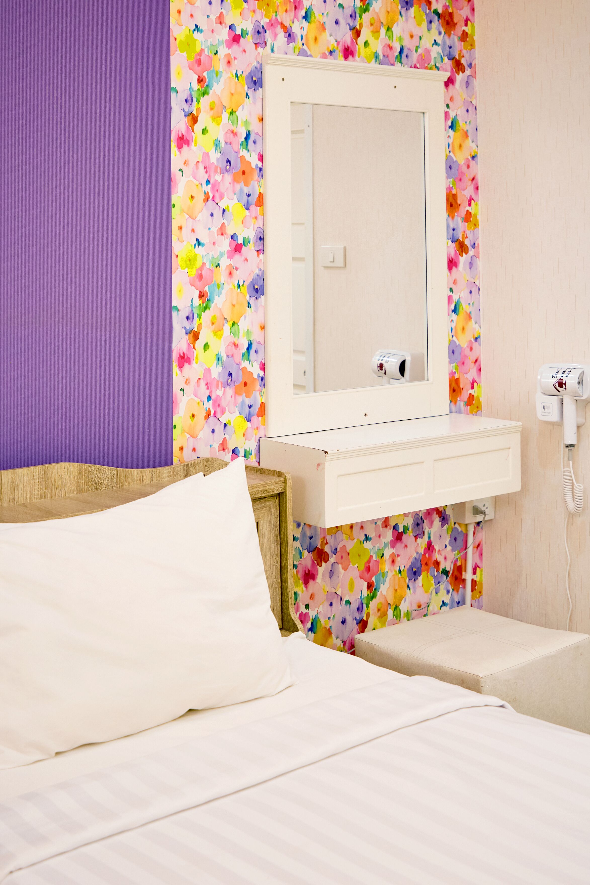 Una habitación de hotel con una cama, una mesita de noche, un espejo y una pared con diseño floral.