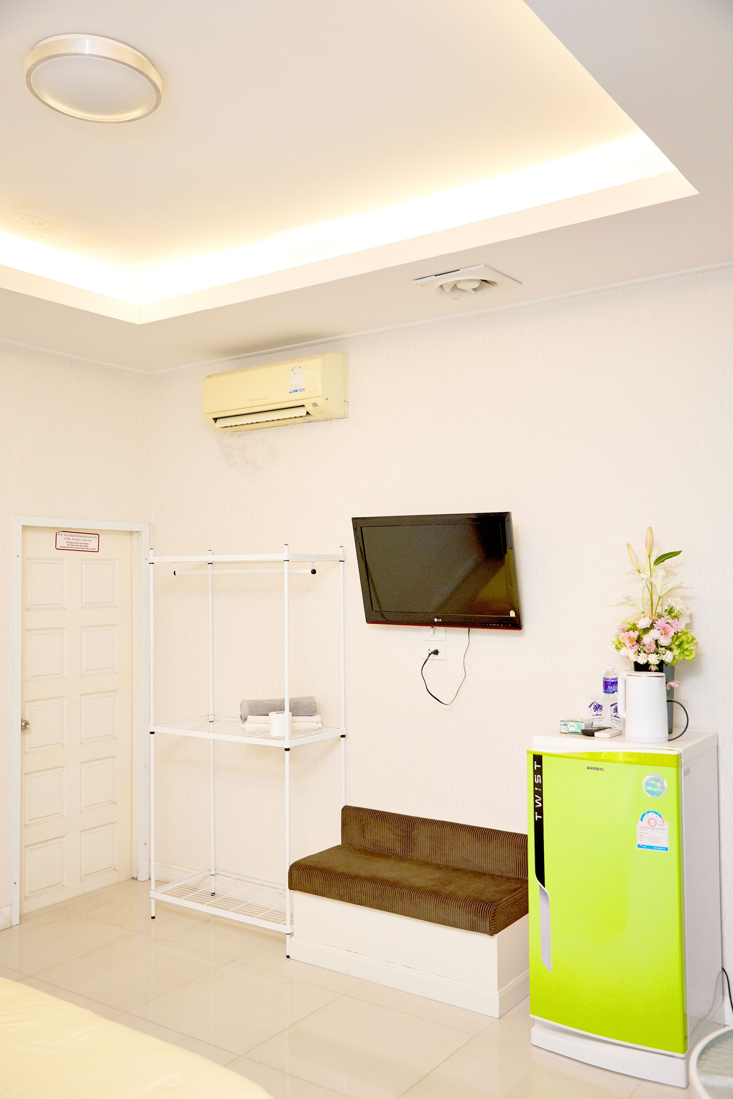 A room with a bed, a TV mounted on the wall, a white air conditioning unit, and a green refrigerator.