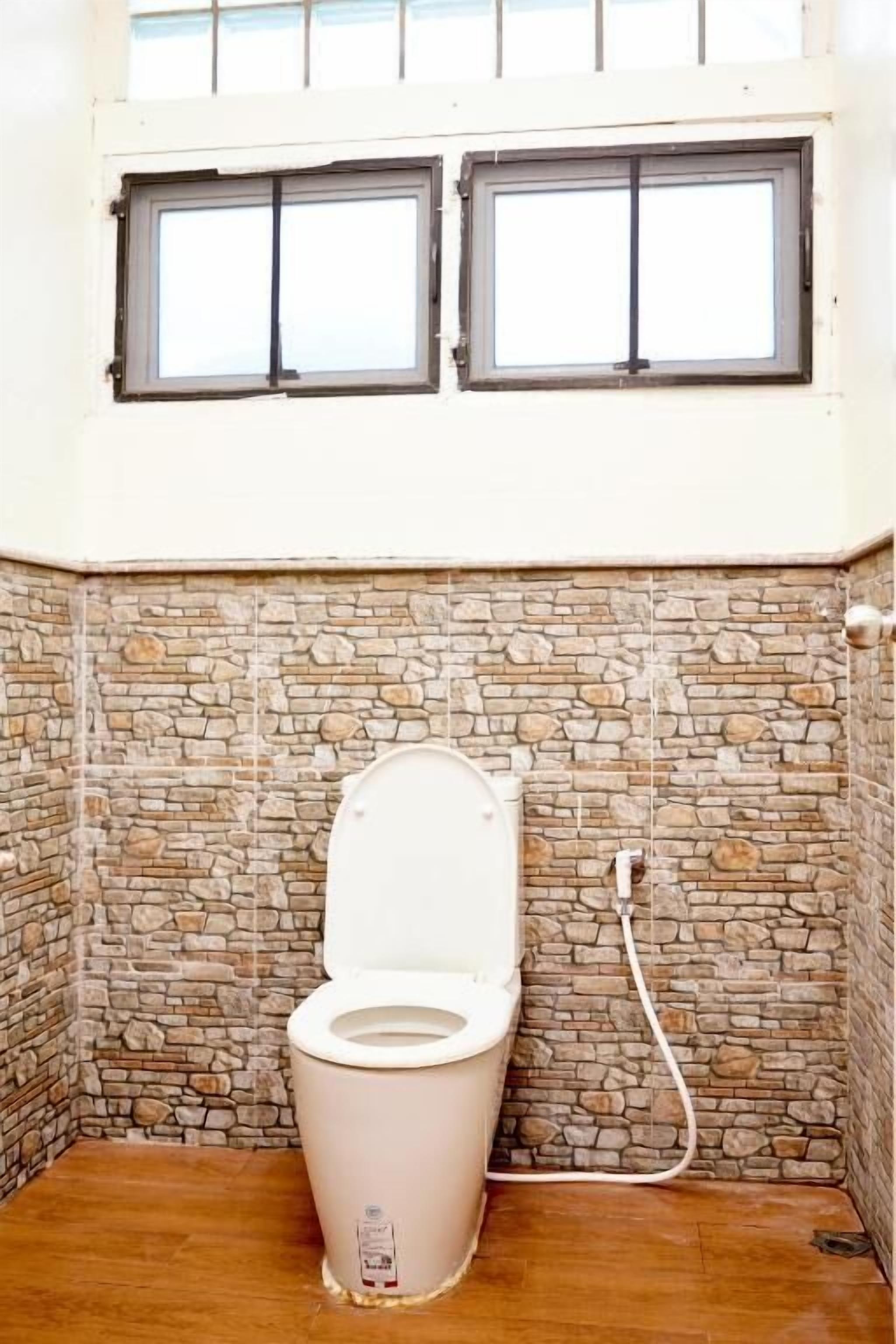 Un baño pequeño con paredes de piedra, un inodoro y una ventana encima.