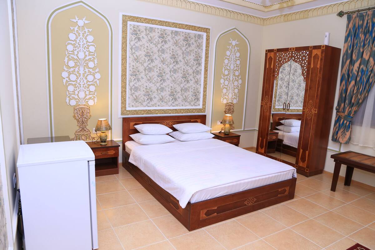 A bedroom with a wooden bed, white bedding, decorative wall panels, and a wardrobe with a mirror.